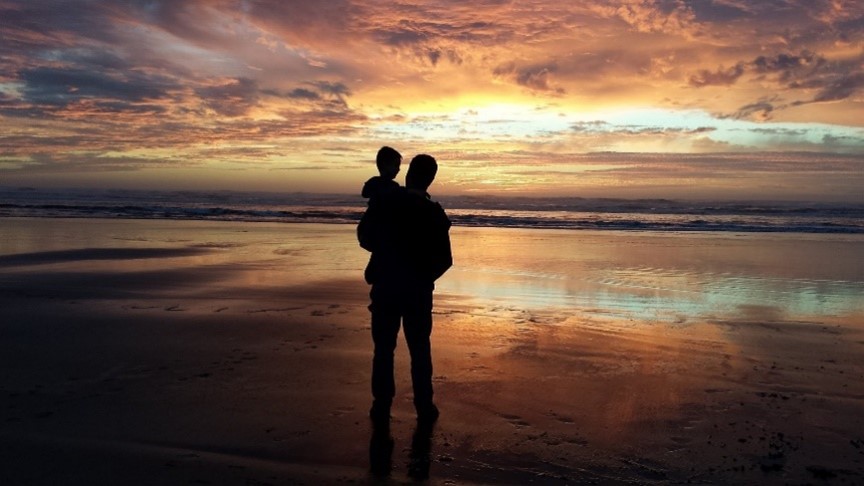 Vater mit Kind vor Sonnenuntergang am Meer